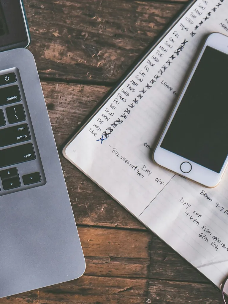 Computer and phone on a table with a planner