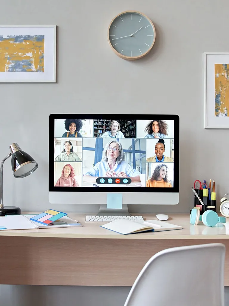 Picture of a computer screen on a writing desk. On the screen is a digital meeting.